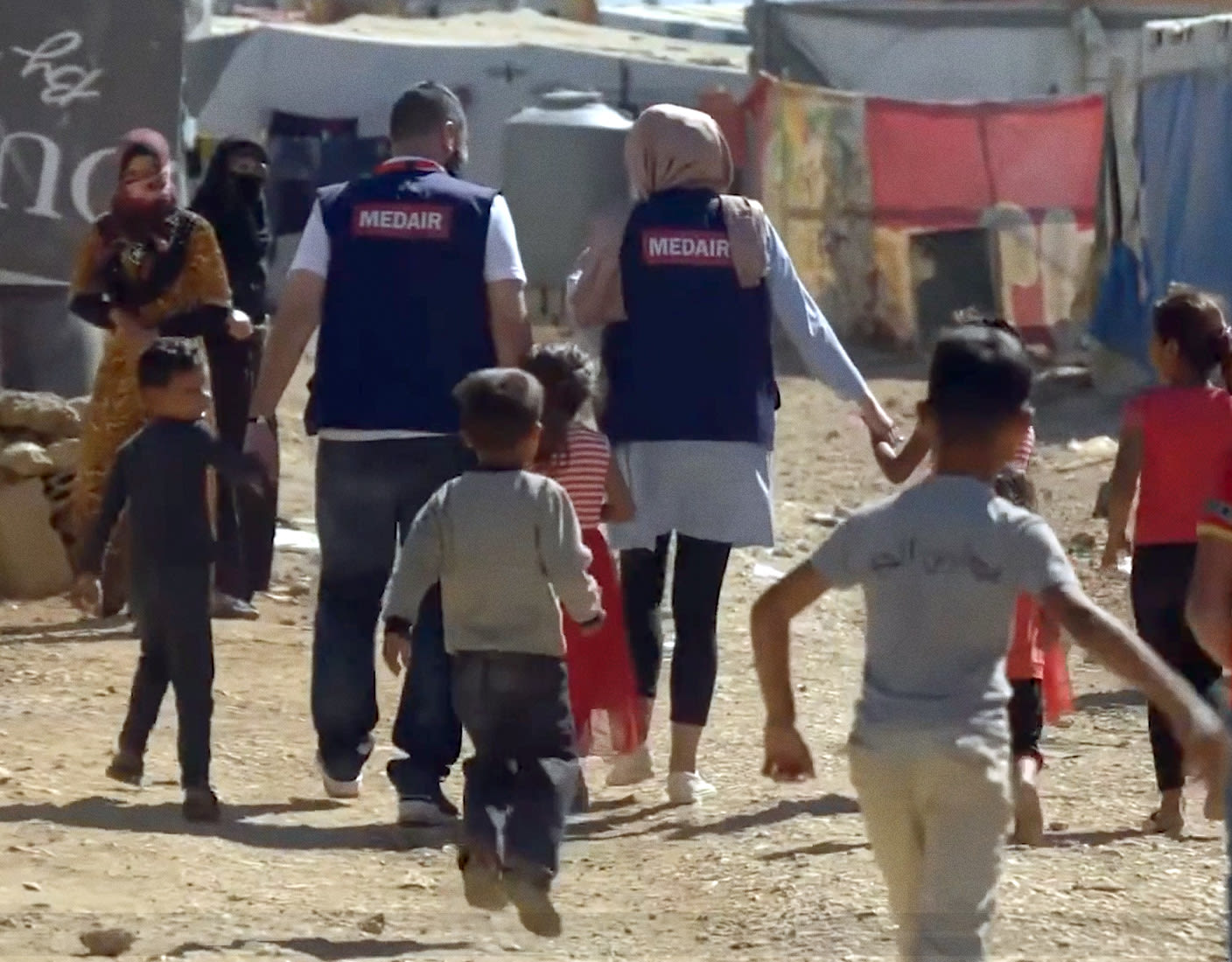 A group of children walking along a dirt road, passing tents, as Medair workers provides essential support in remote areas.